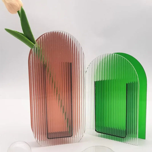Two modern acrylic vases, one pink and one green, tall and short ,on a light grey background.