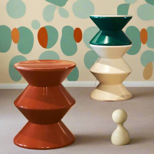 Two geometrically designed stools in a living room setting with a gray sofa and green chair.