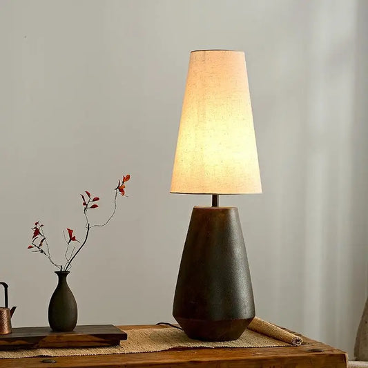 Table lamp with a warm glow on a wooden surface next to a small vase and decorative items.