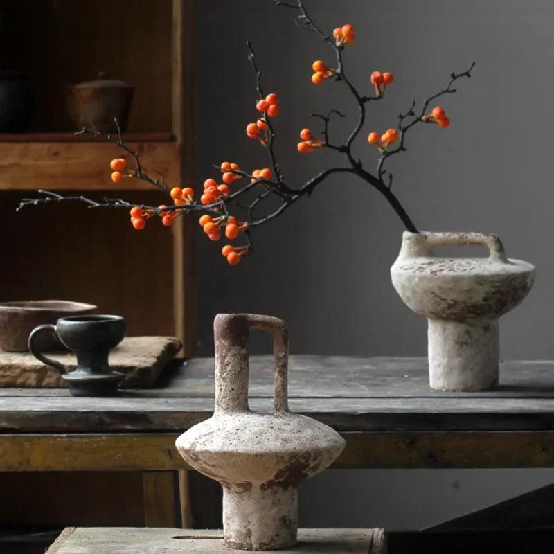 Decorative arrangement with branches and orange berries on a rustic wooden table.
