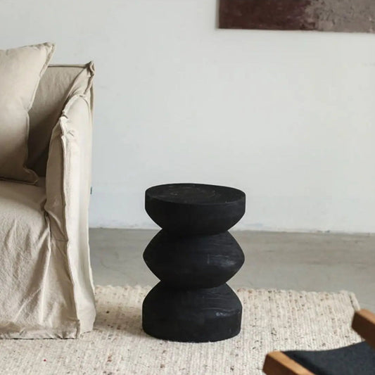 Black carved wabi sabi japanese stool in a minimalistic living room setting with a neutral color palette.