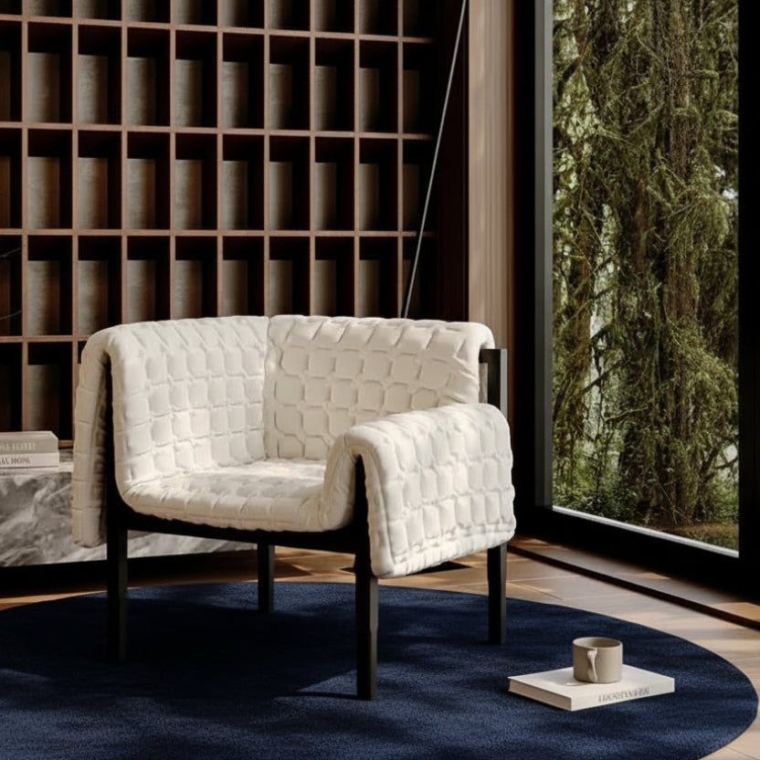 White quilted armchair in a modern interior setting with a bookshelf and window.