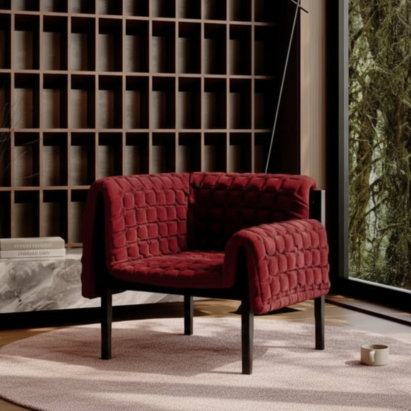 Red quilted armchair in a modern interior setting with a bookshelf and window.