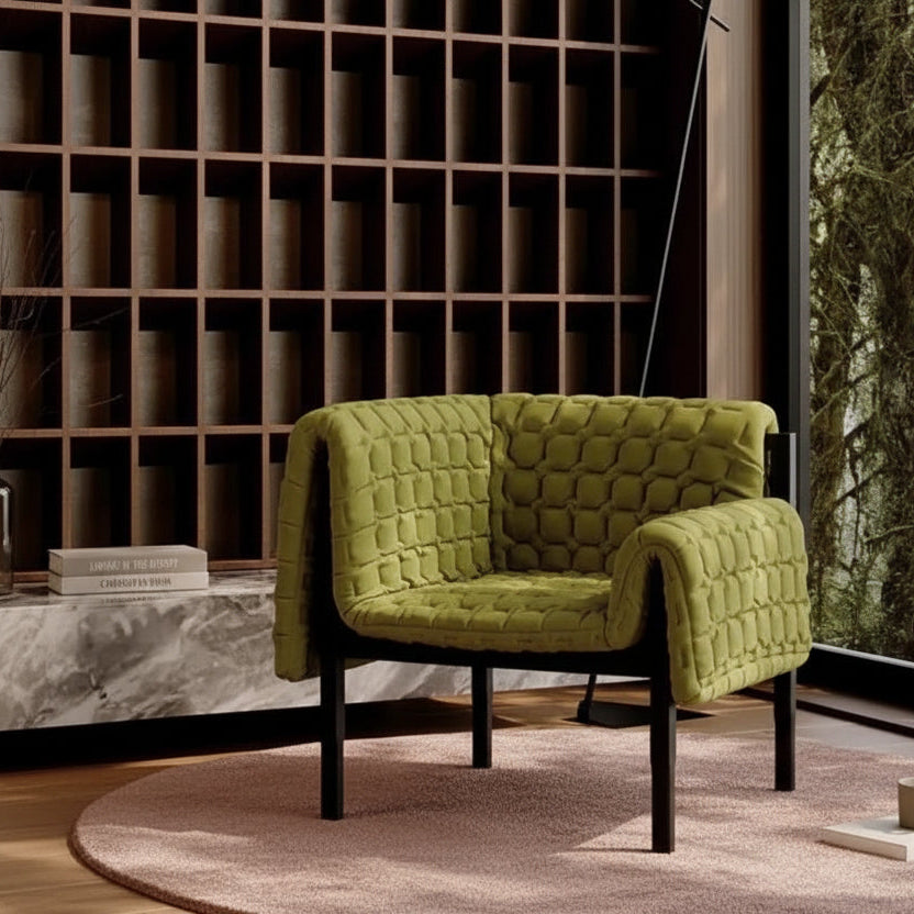 Green quilted sofa in a modern interior setting with a bookshelf and window.