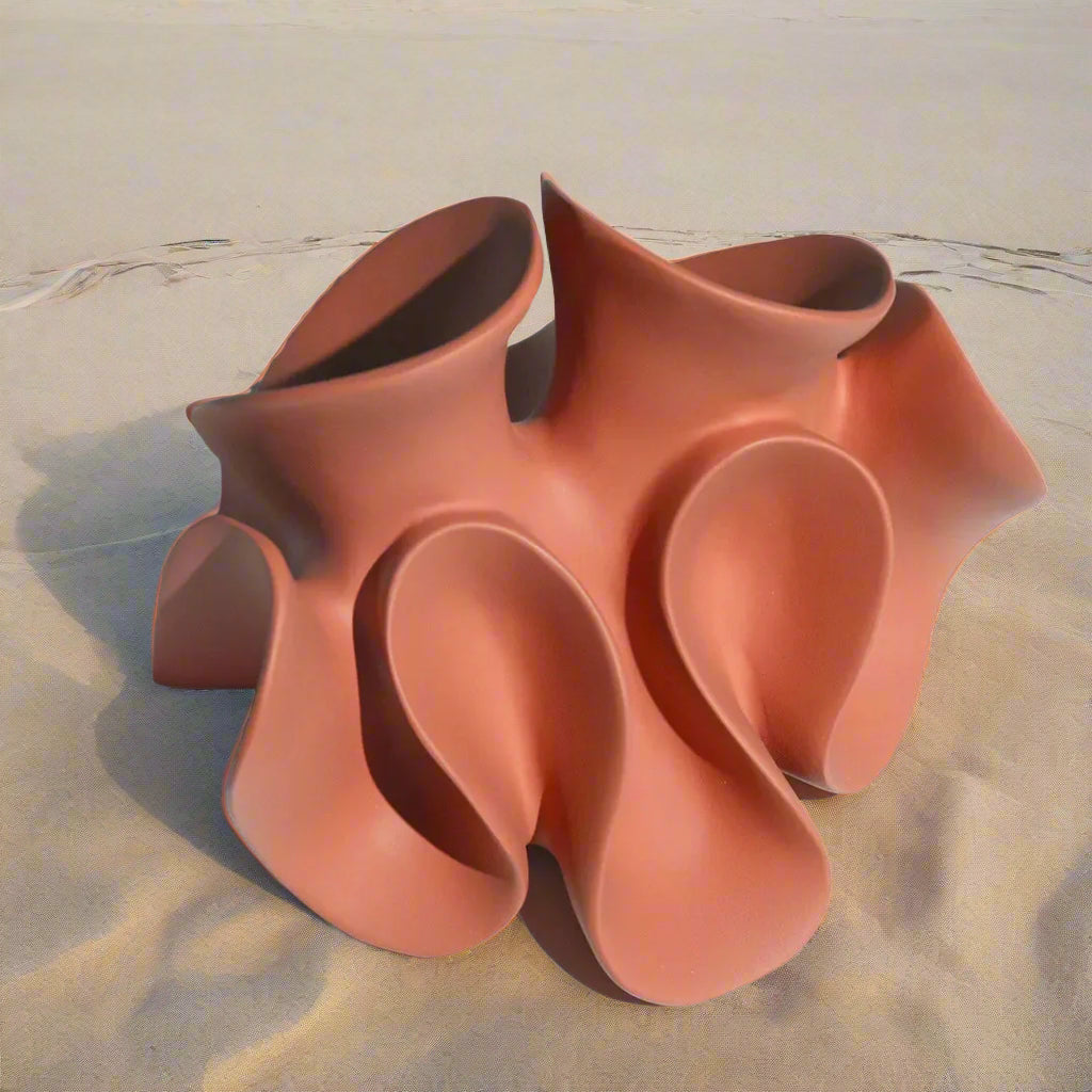 Soft coloured orange resin sculpture with wavy design on a light bench top