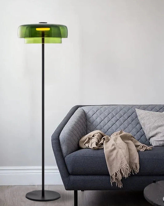 Green floor lamp next to a gray sofa with a beige blanket in a minimalistic room.