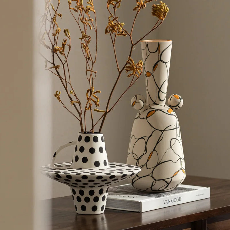 Two ceramic vases on a wooden surface with a book underneath, against a neutral background.