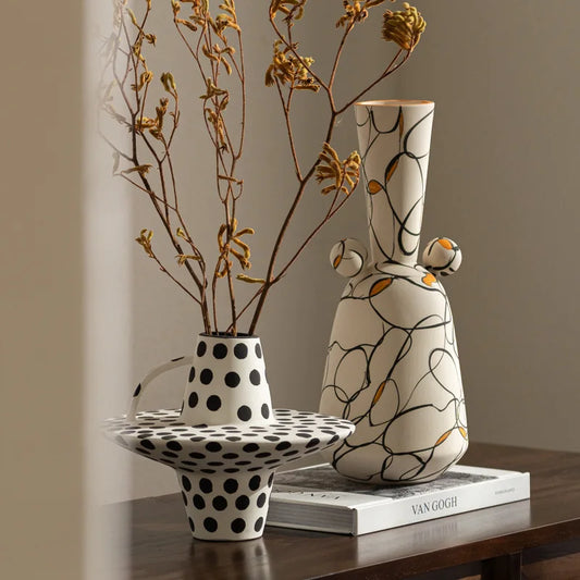 Two ceramic vases on a wooden surface with a book underneath, against a neutral background.