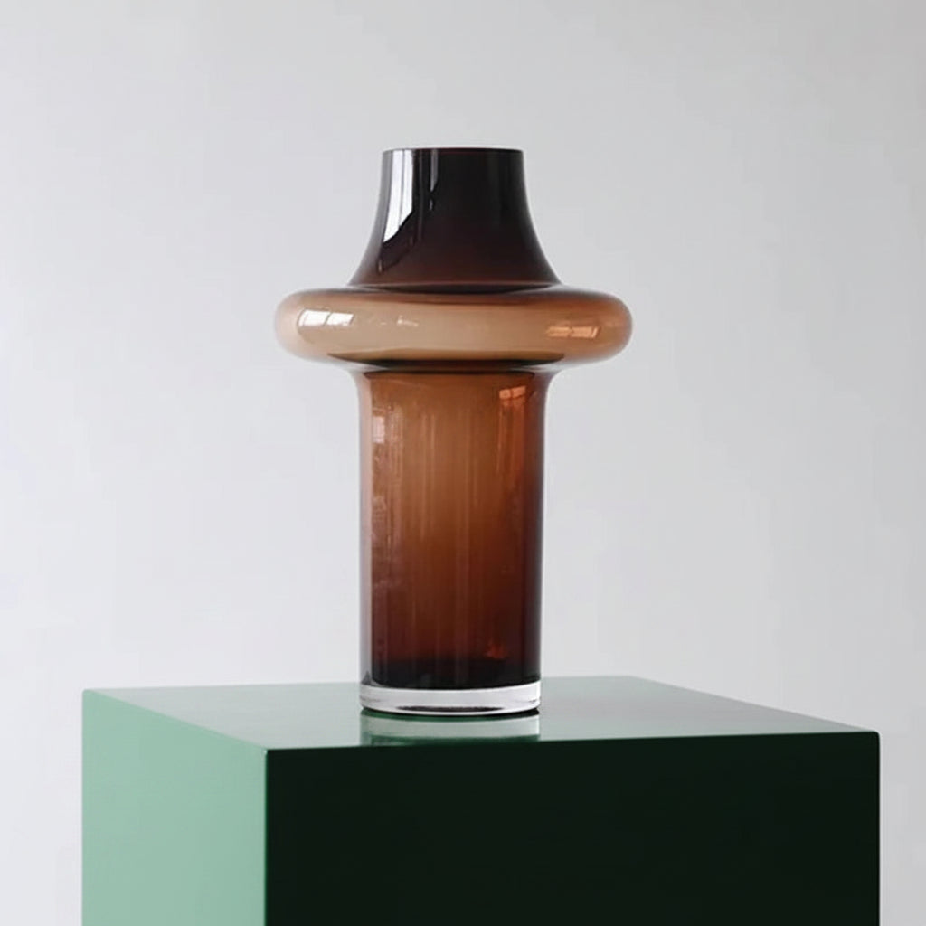 Brown glass vase with a black top on a white pedestal against a light gray background