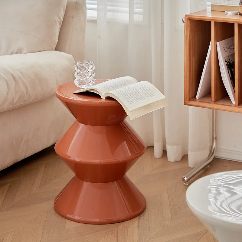 Orange side table with a book and glass on a wooden floor next to a beige sofa.