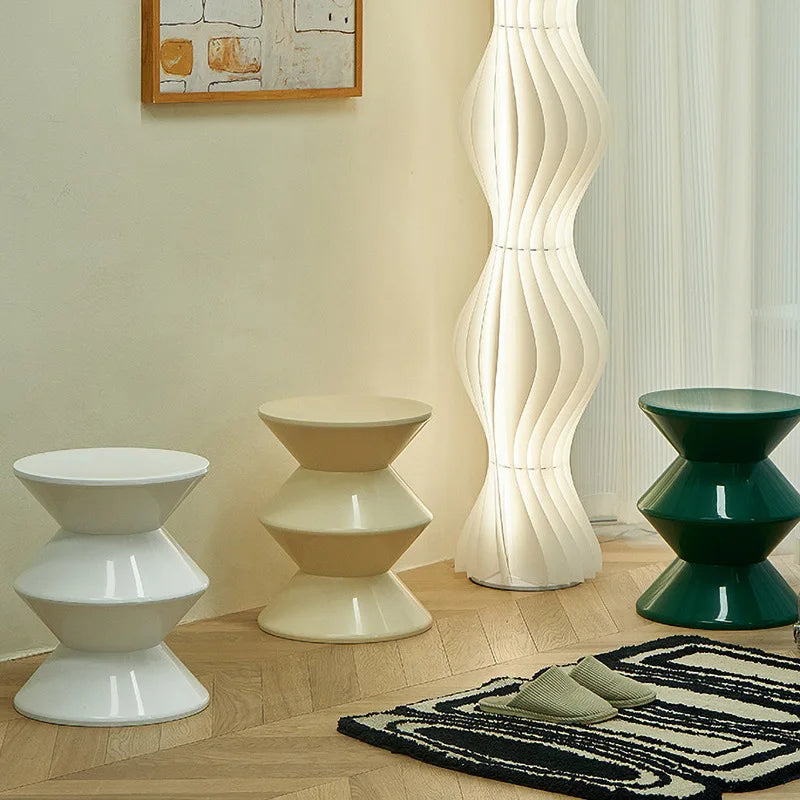 Three modern stools in white, beige, and green with a floor lamp in the background.