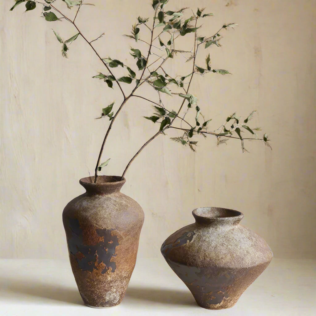 Two rustic ceramic vases with a branch on a plain background