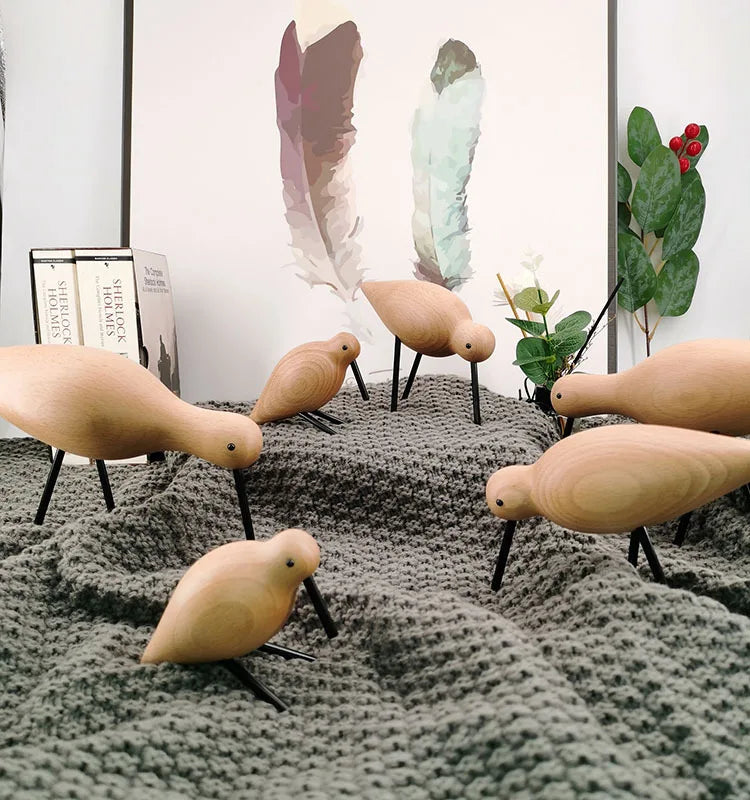 Wooden bird sculptures on a textured surface with books and plants in the background